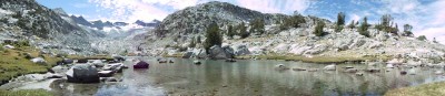 A hundred feet of shallow pond lie in front of me, flowing rightward to narrow and flow down; in front is an outcropping of rock, and somewhat to the left and back lie mountains with snow-covered flanks