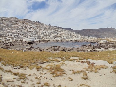 A desolate, late-summer alpine pool surrounded by granite rocks