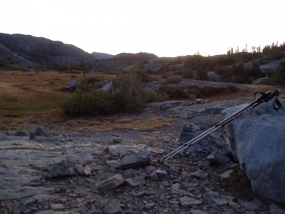Hiking poles lean against a rock in the foreground, while in the background brightness limns the surrounding hills